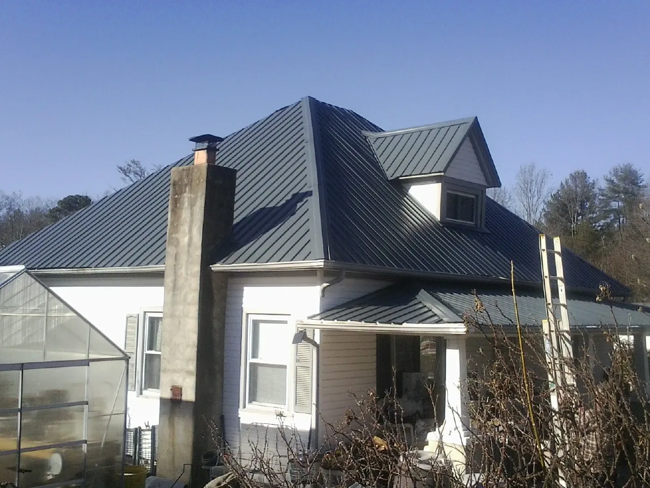 Dark blue standing seam metal roof on a white farmhouse with dormer — Slate & Tile Roof Repair by Roofing Brothers in Wahpeton