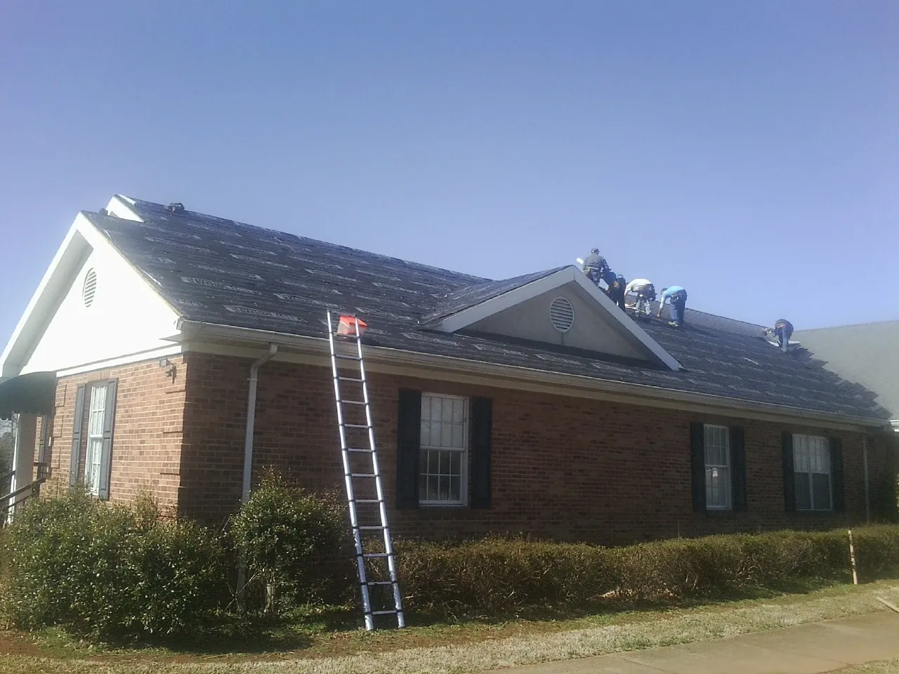 Crew tearing shingles off a brick ranch roof with a ladder set — Metal Roof Repair work by our crew in Wahpeton