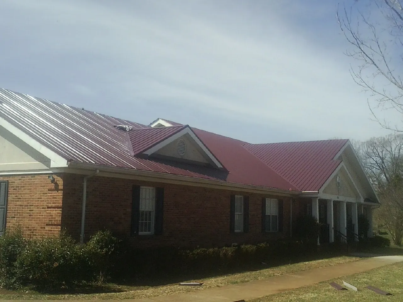 Red metal roof with gabled entries on a long brick building, from a Hail Damage Roof Repair job in Wahpeton