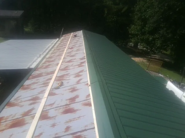Old rusted panels beside newly installed green metal roofing — Wind Damage Roof Repair by Roofing Brothers in Wahpeton