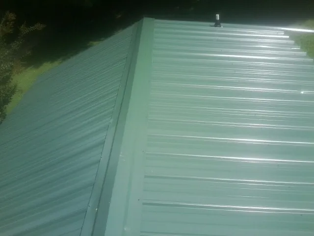 New green metal panels meeting at the ridge of a roof — Flat Roof Repair work by our crew in Wahpeton