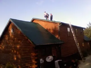 Crew on the ridge of a green metal roof on a two story log home in Wahpeton