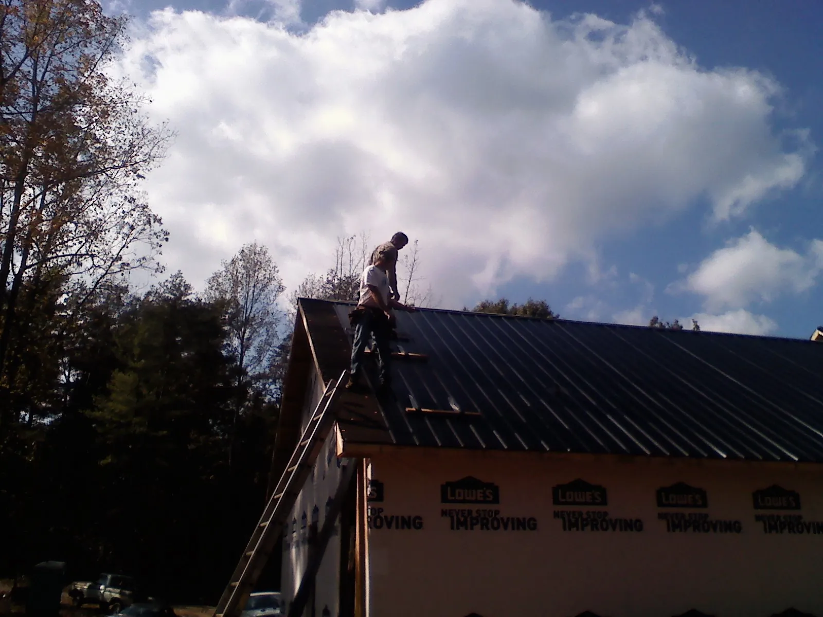 Roofer fastening dark metal panels high against a cloudy sky, from a Roof Inspection job in Wahpeton