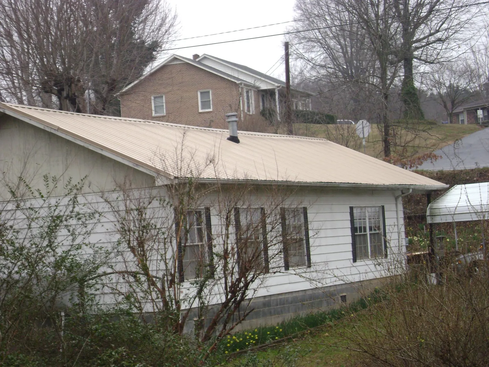 Tan metal roof on a white sided house set into a hillside — Commercial Roofing by Roofing Brothers in Wahpeton