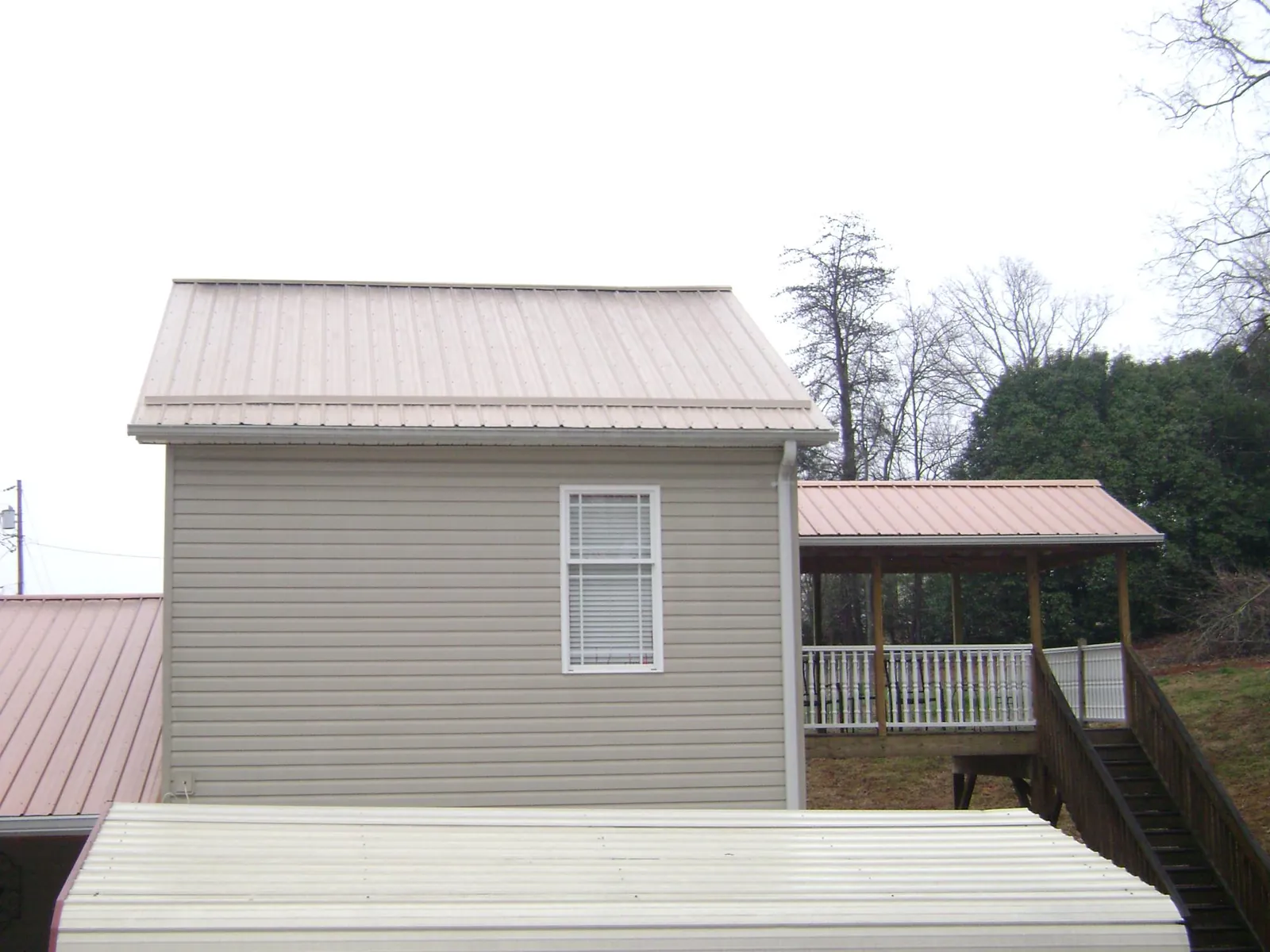 Tan metal roofs on a two story addition and attached porch, from a Roof Replacement job in Wahpeton